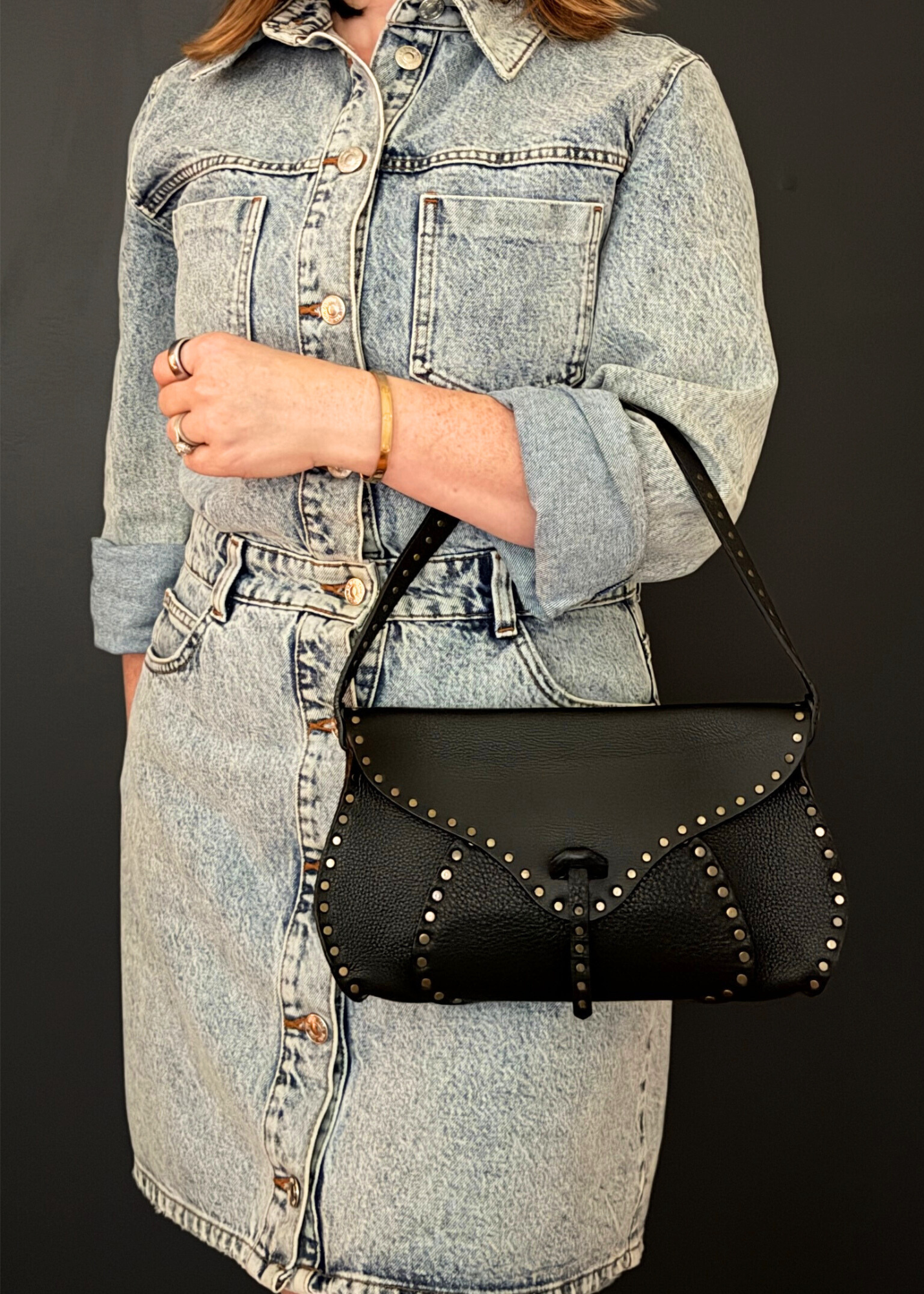 Person wearing a denim jacket holding a vintage Celine black studded handbag against a dark background