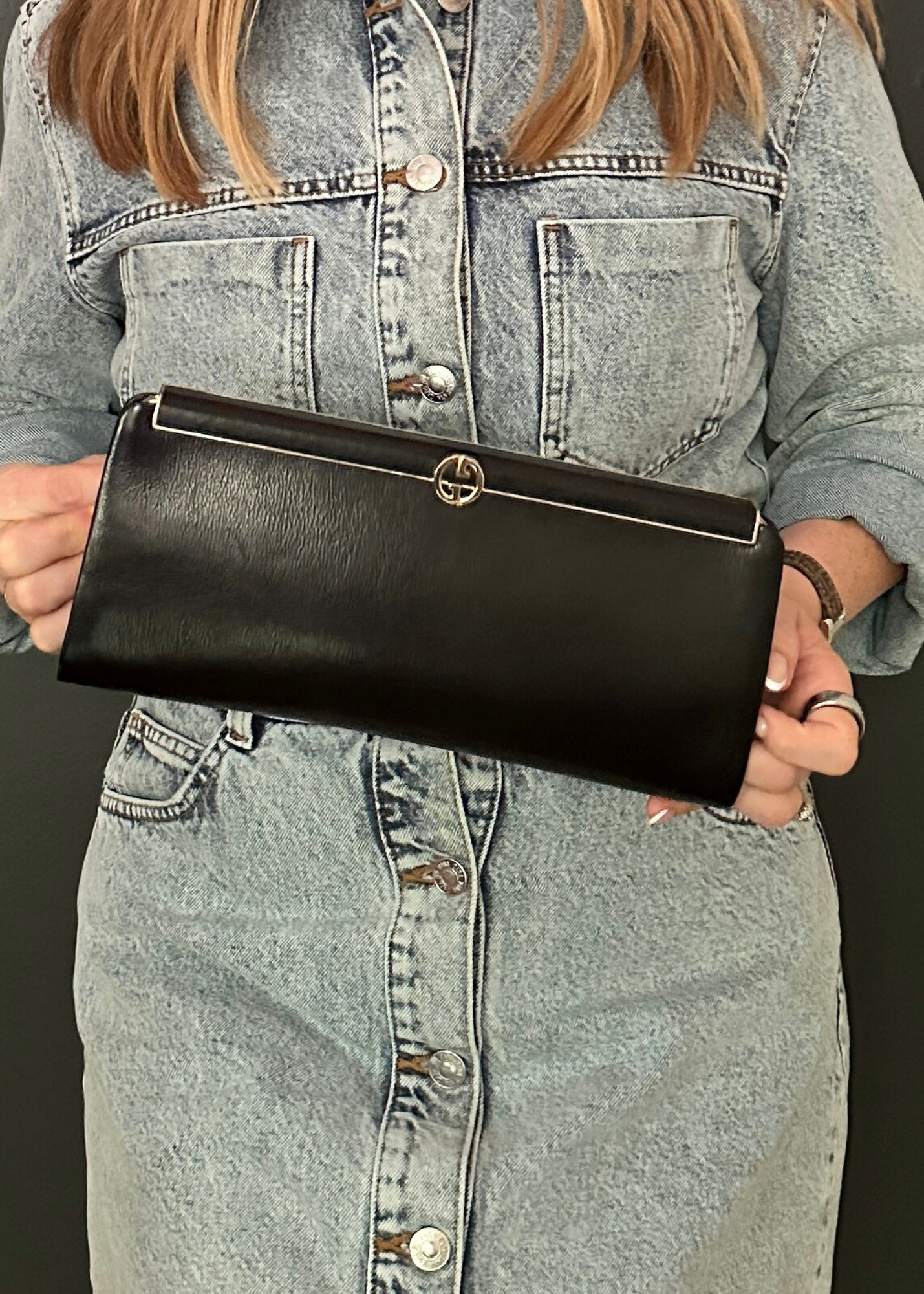 Person holding a black Gucci clutch with a denim dress