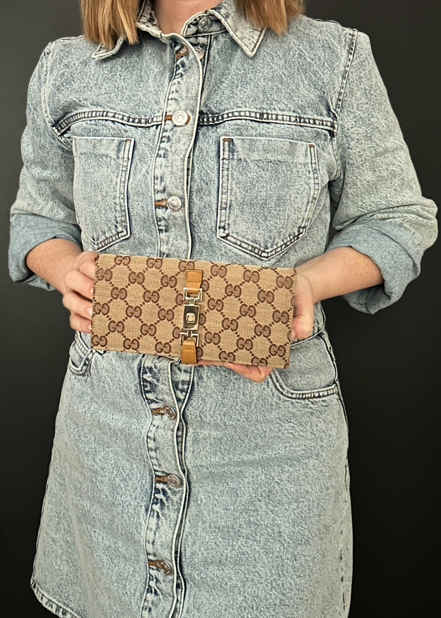 Person wearing a denim jacket holding a Gucci handbag against a black background