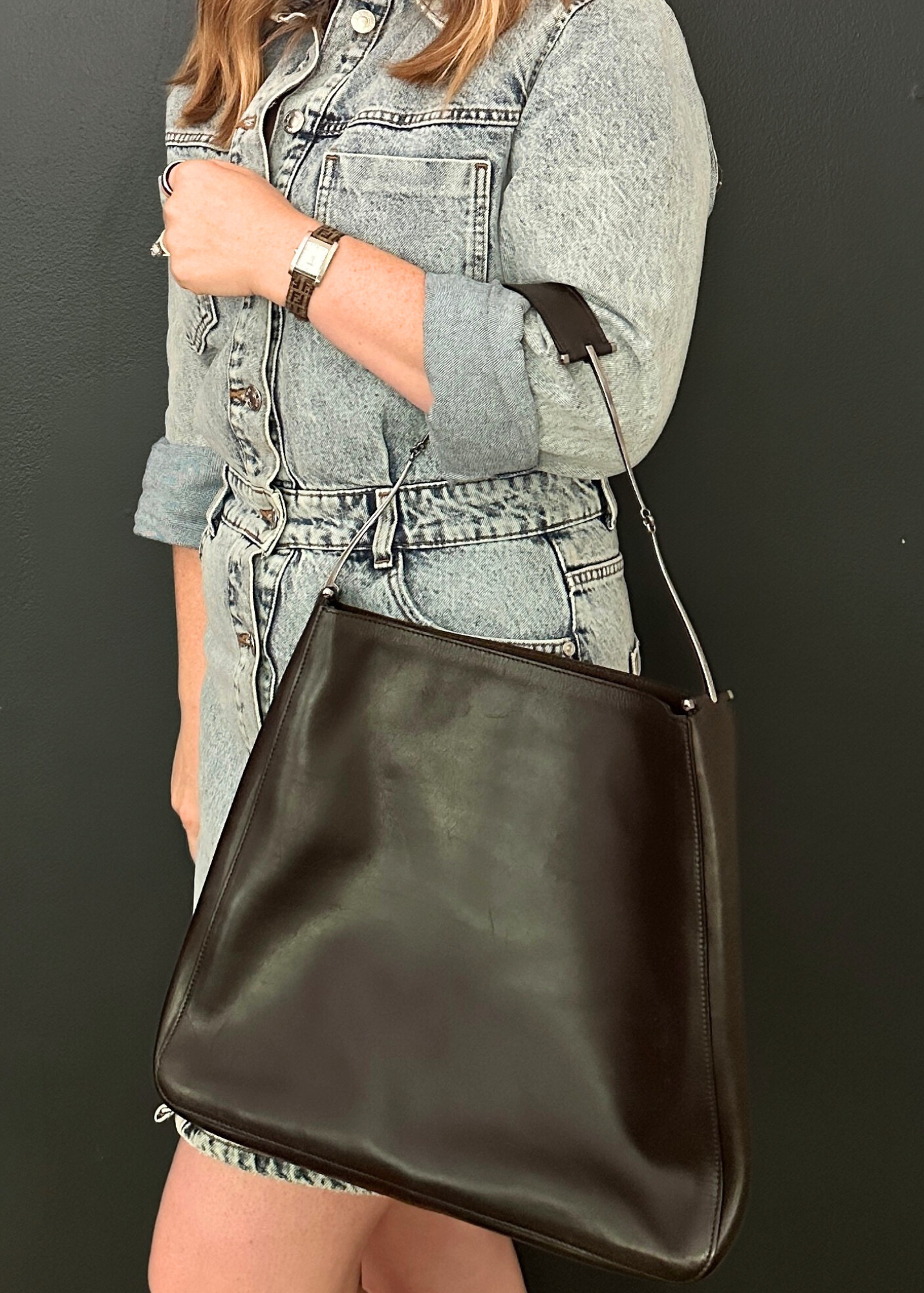 Person holding a dark brown leather handbag against a plain background