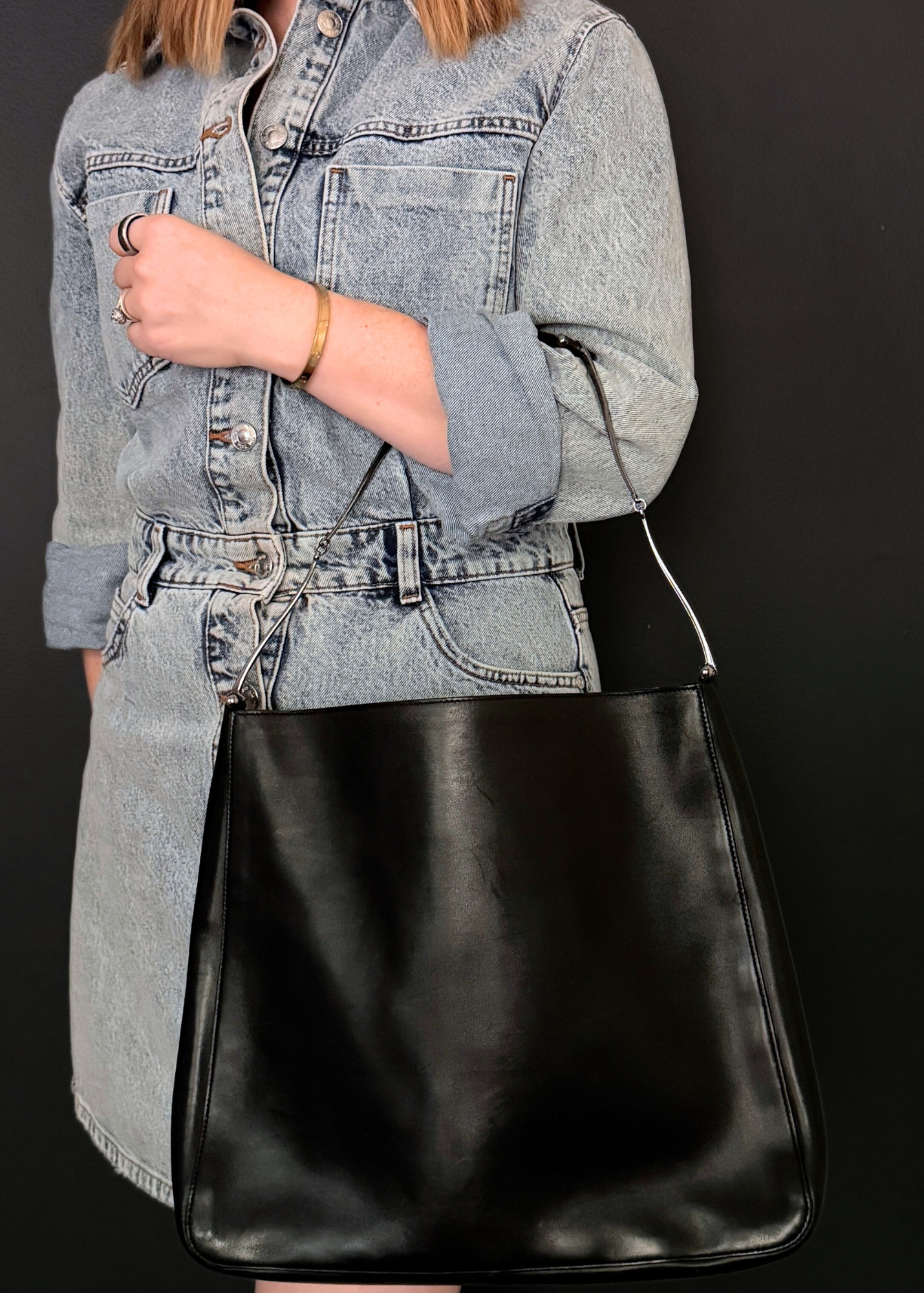 Person wearing a denim jacket holding a vintage Gucci black leather bag against a dark background