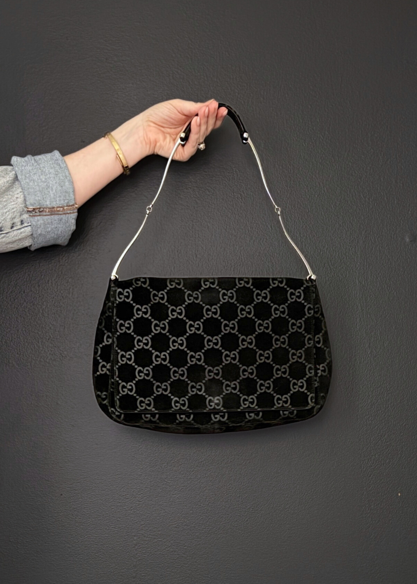 Black vintage Gucci handbag with a GG monogram pattern held by a person against a dark background