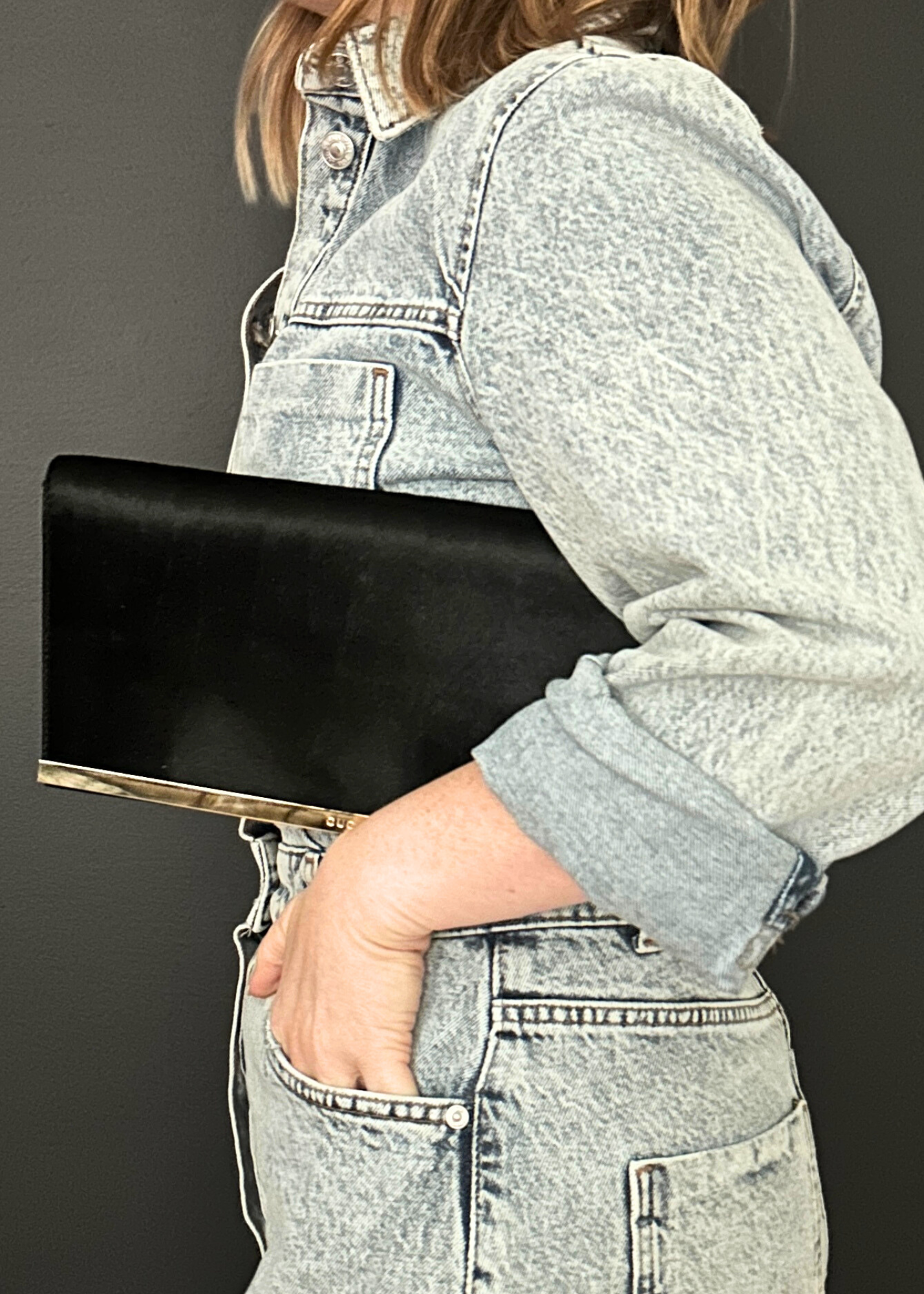 Person holding a black vintage Gucci clutch bag against a plain background