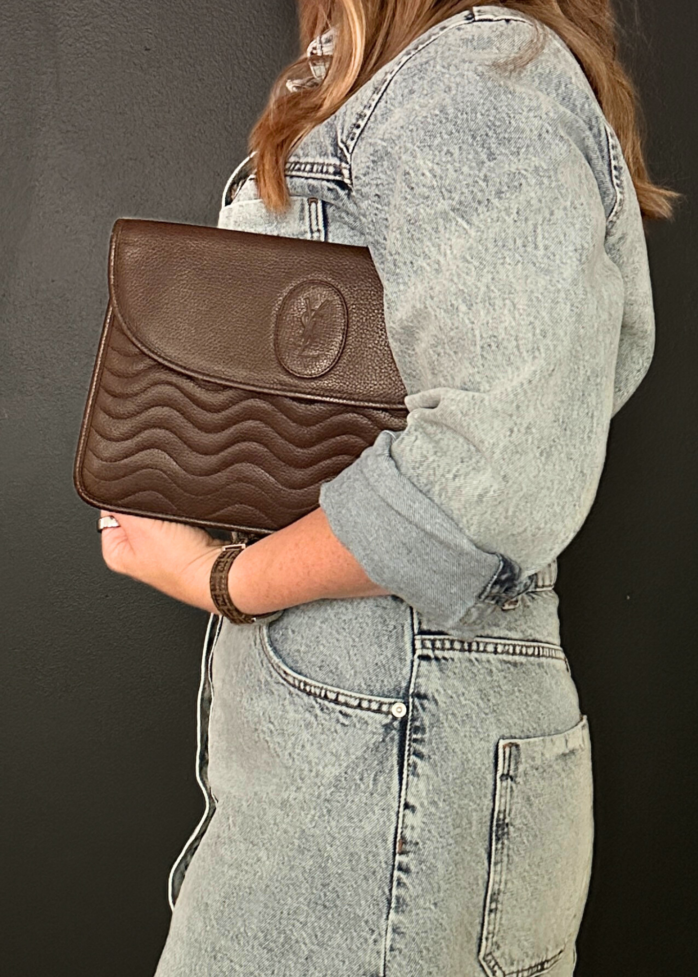 Person holding a brown clutch with a textured surface against a dark background