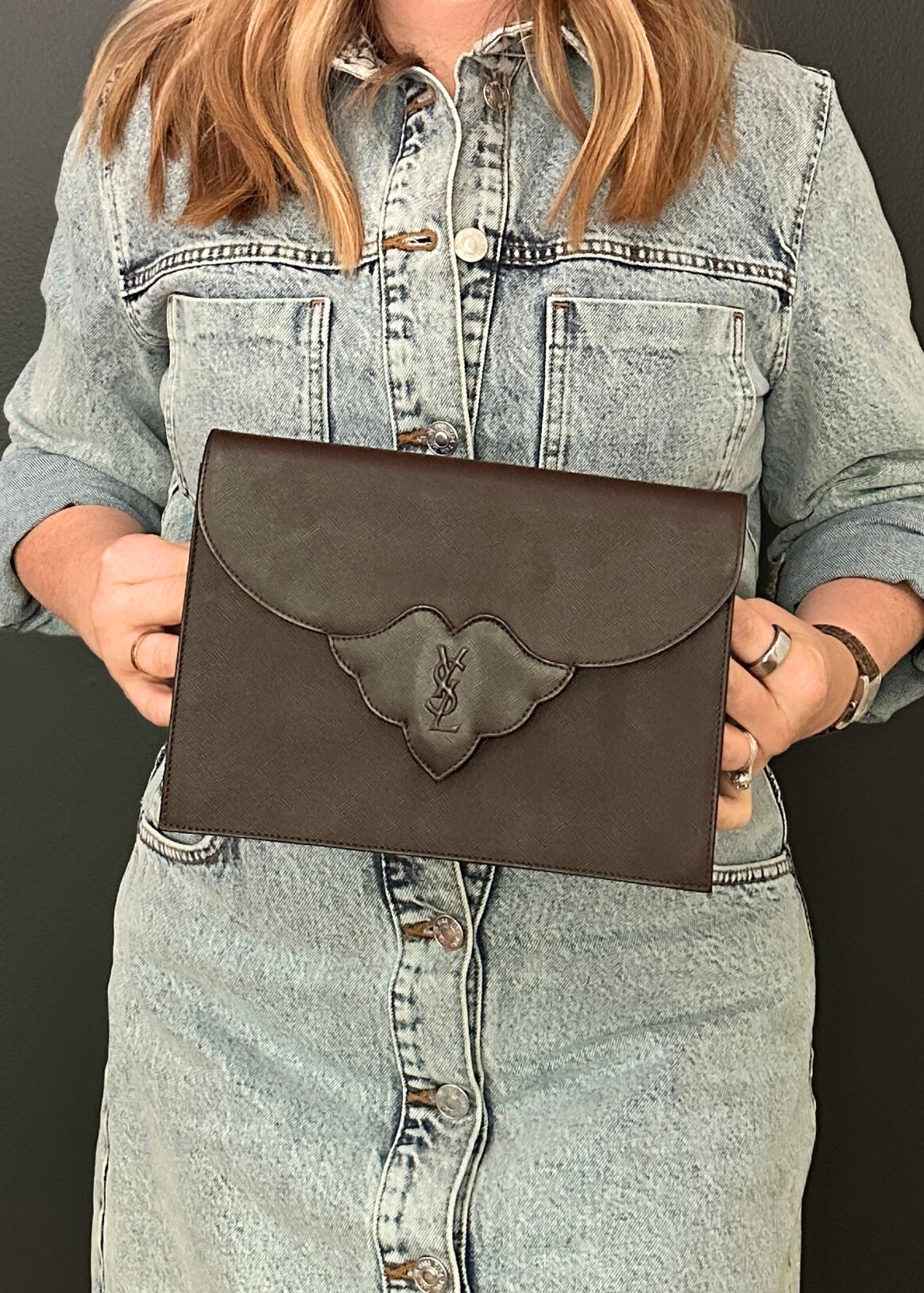 Person holding a brown leather clutch against a dark background