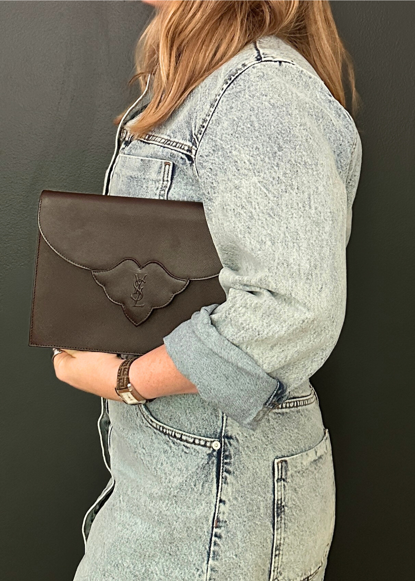Person holding a brown clutch with a brand logo against a dark background
