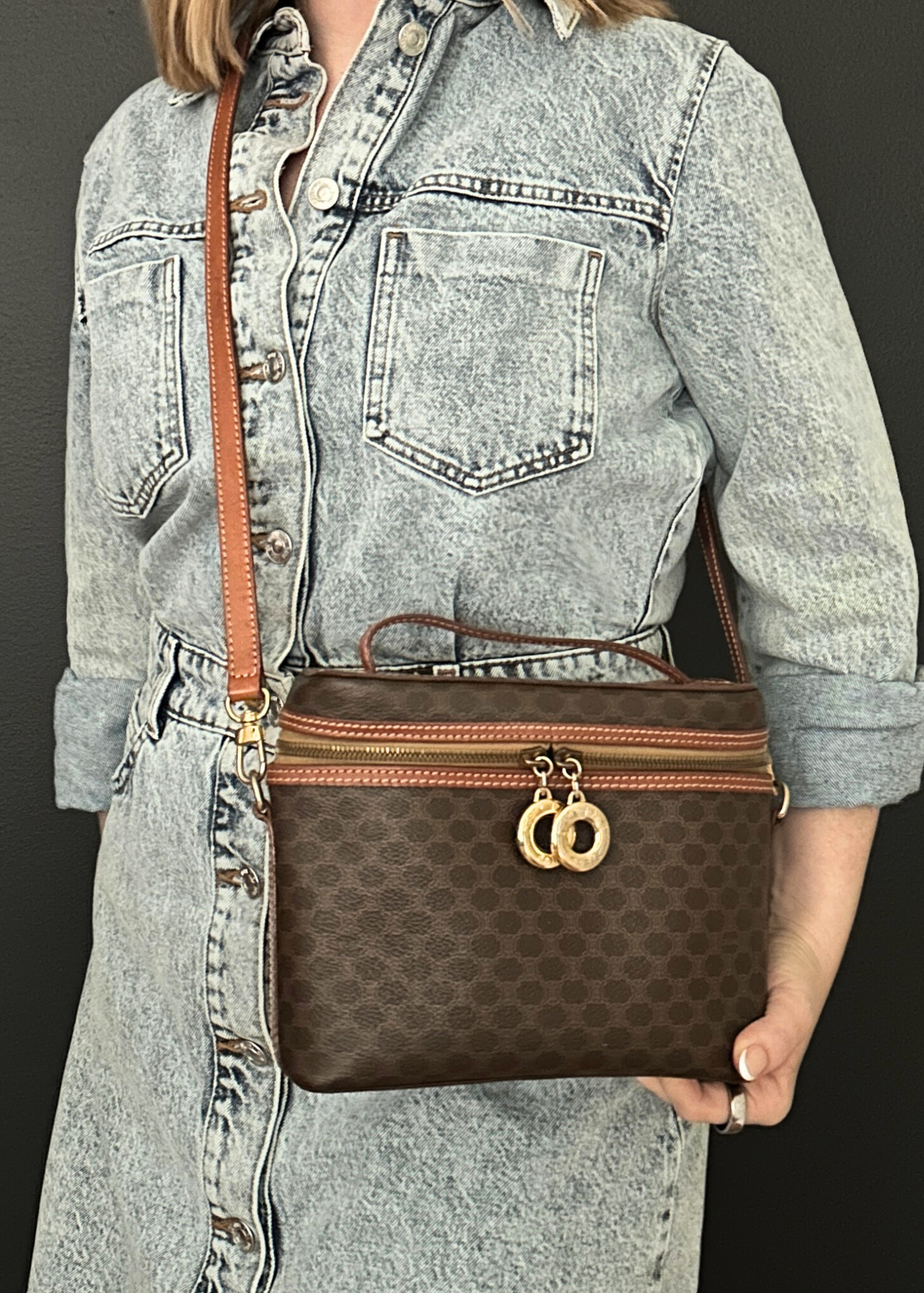 Person holding a brown Celine handbag with a patterned strap against a dark background