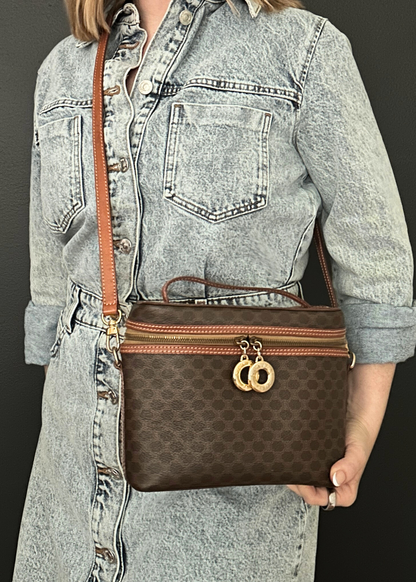 Person holding a brown Celine handbag with a patterned strap against a dark background