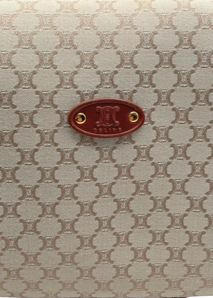 Close-up of a vintage Celine handbag featuring the brand's signature repeating triomphe monogram pattern in beige and brown, with a central brown leather oval logo badge.
