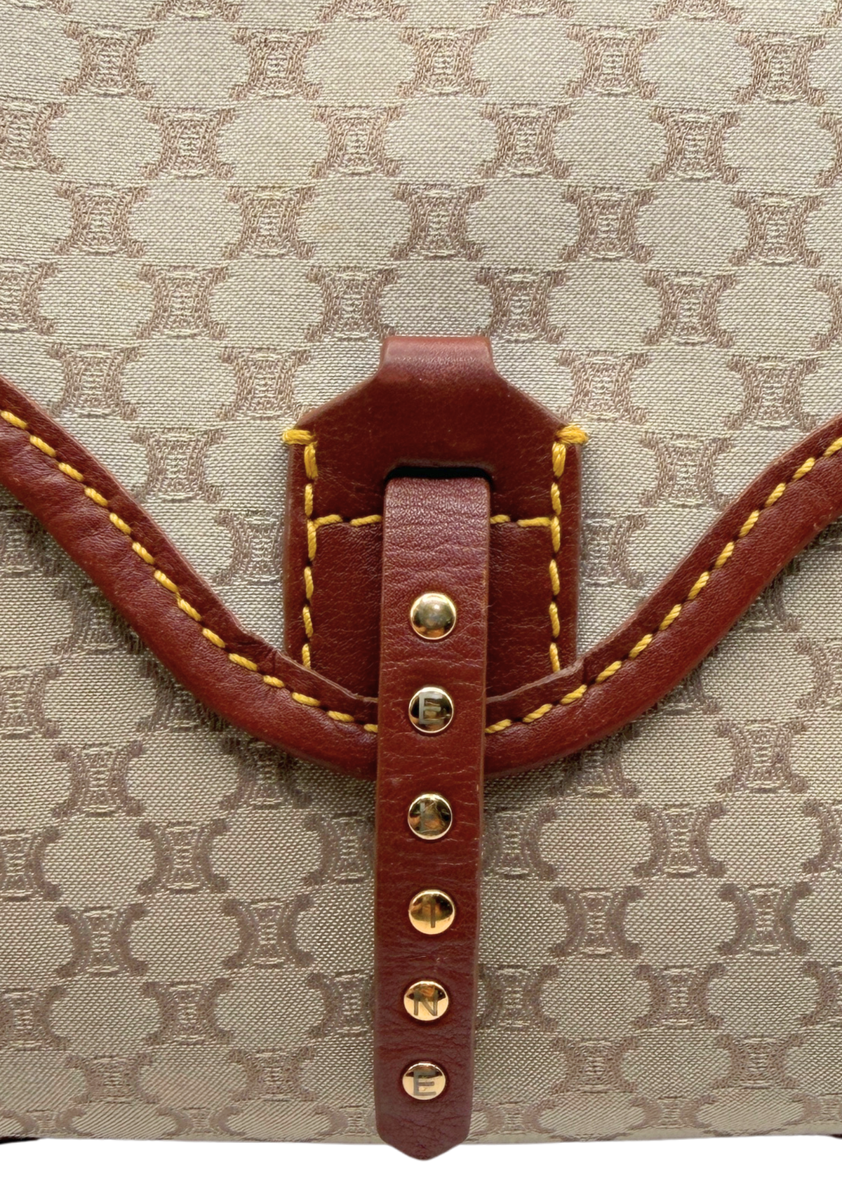 Close-up of a beige and brown vintage Celine triomphe monogram canvas bag with a brown leather strap closure and gold-tone studs.