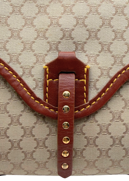 Close-up of a beige and brown vintage Celine triomphe monogram canvas bag with a brown leather strap closure and gold-tone studs.