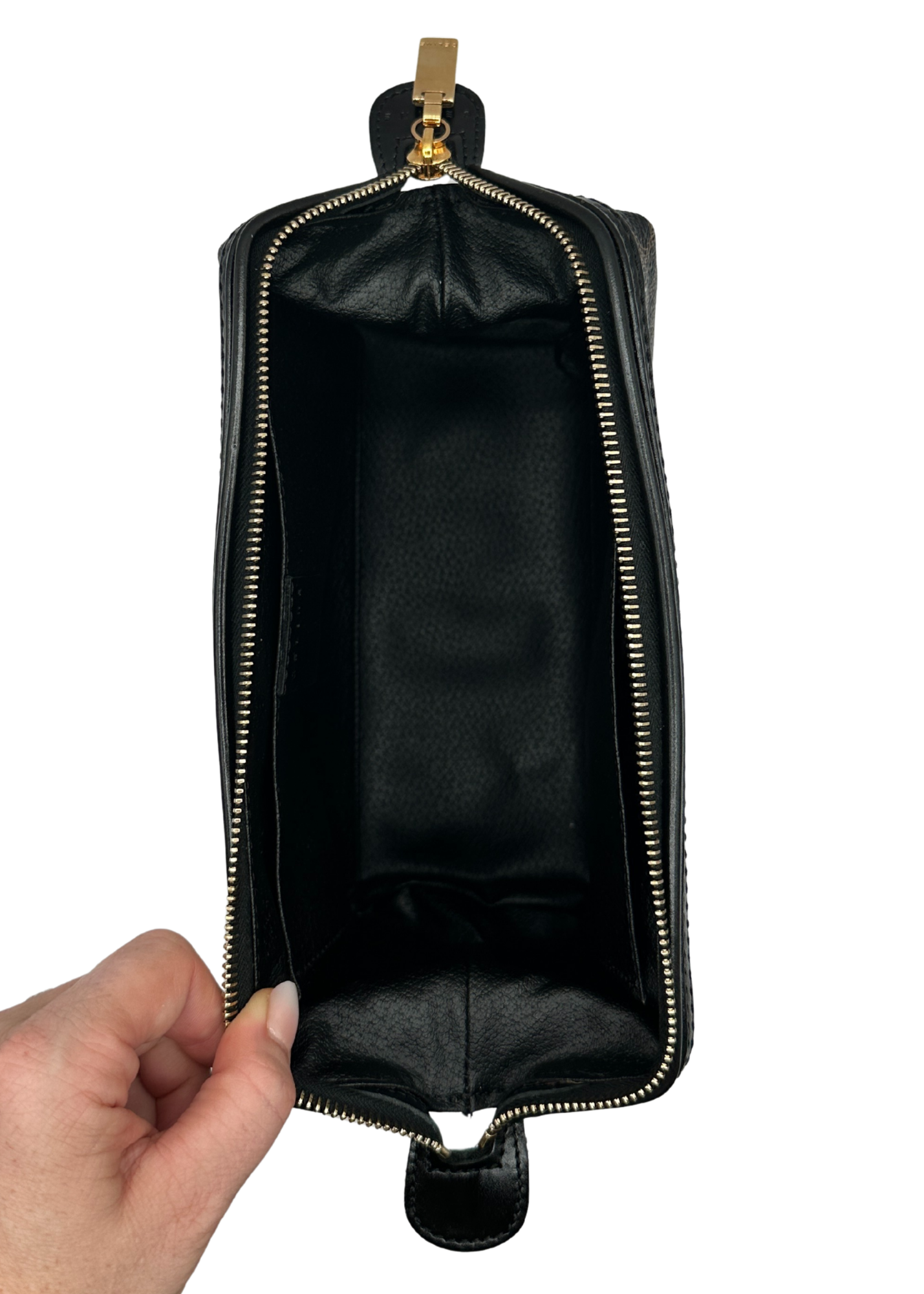 Black leather pouch with gold zipper held open by a hand on a white background