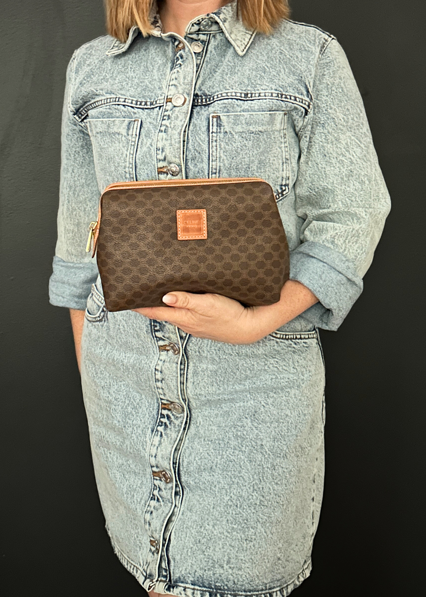 Person holding a brown Celine clutch bag against a black background