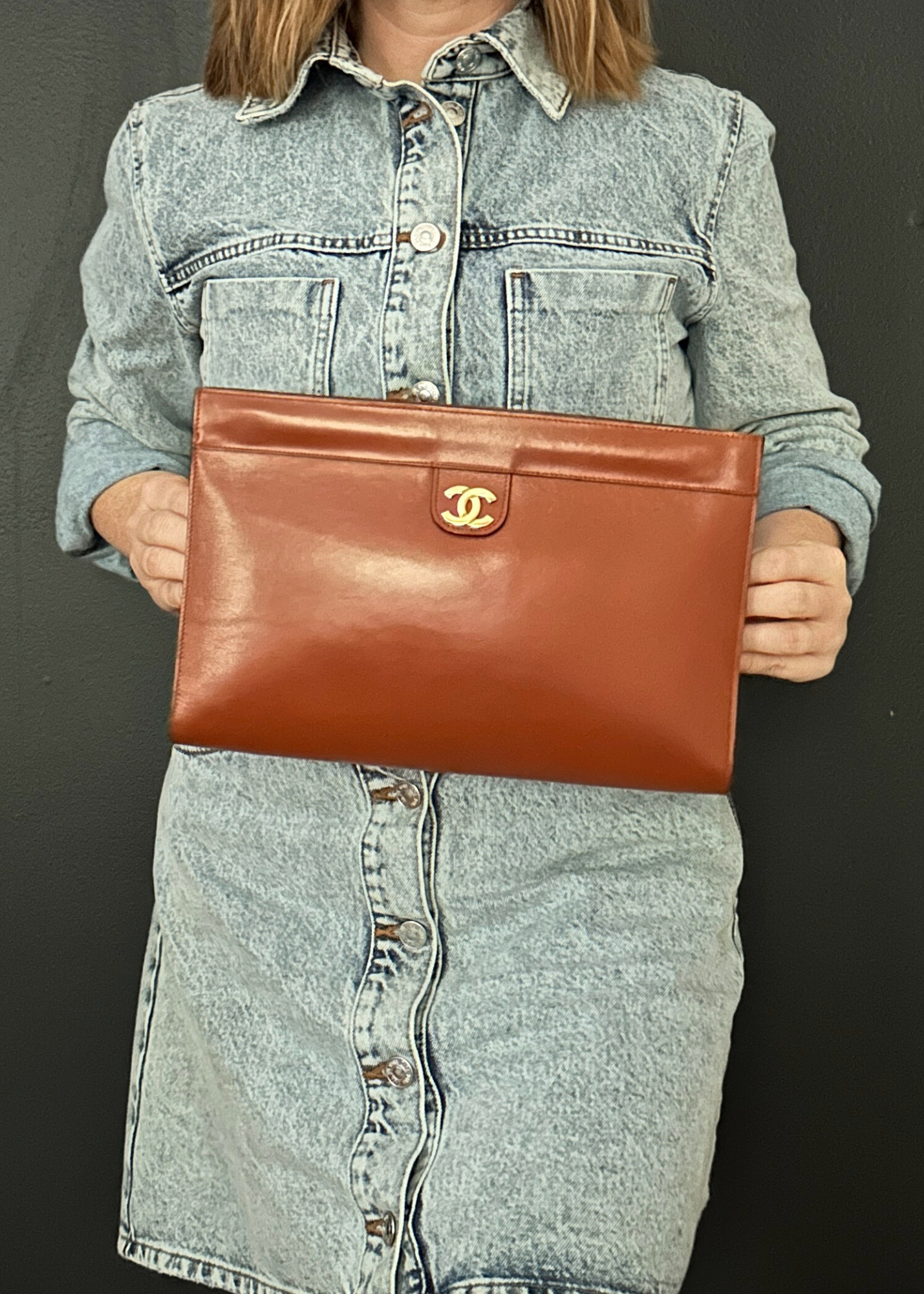 Person holding a vintage Chanel brown leather clutch with a visible brand logo against a dark background