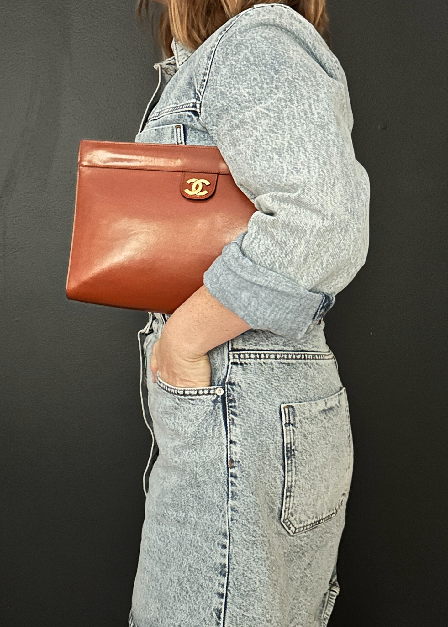 Person holding a brown vintage Chanel leather handbag with a visible brand logo against a dark background