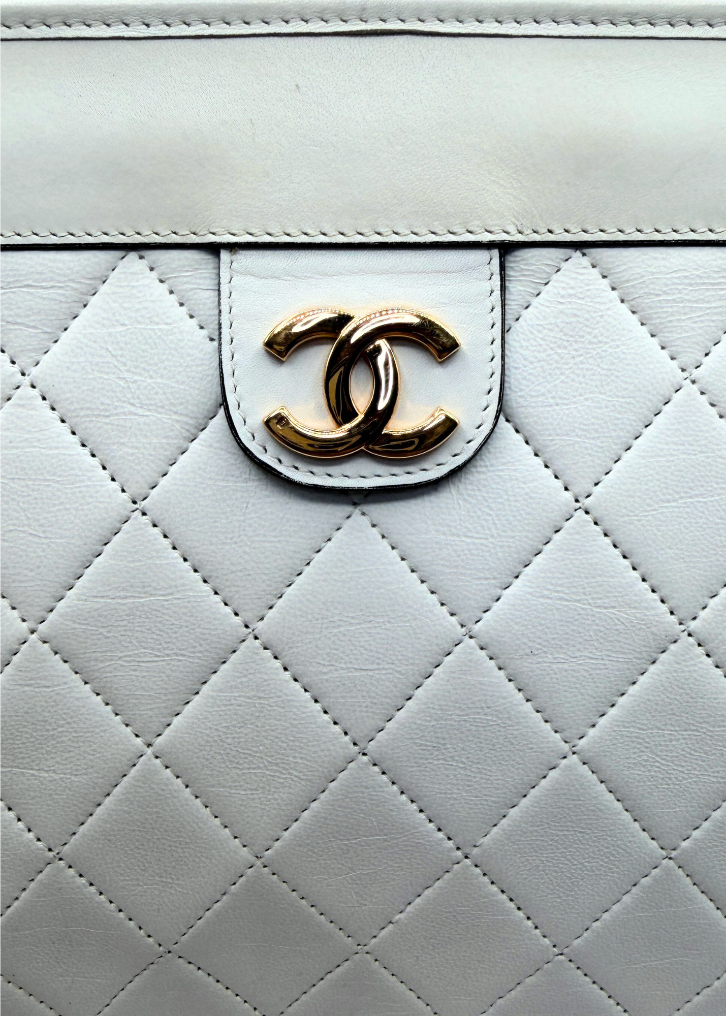 Close-up of a quilted white vintage clutch with a 24k gold Chanel logo.
