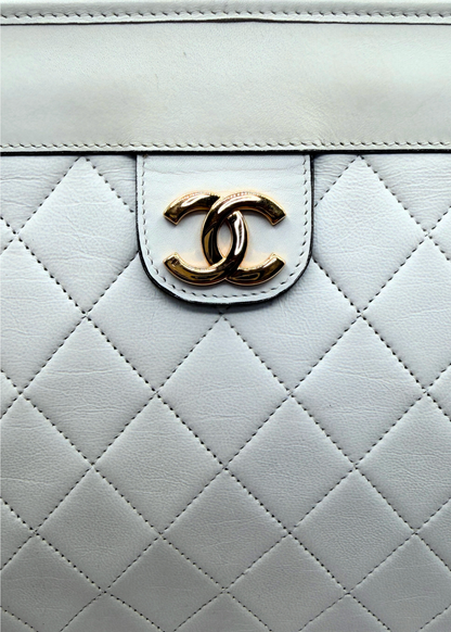 Close-up of a quilted white vintage clutch with a 24k gold Chanel logo.