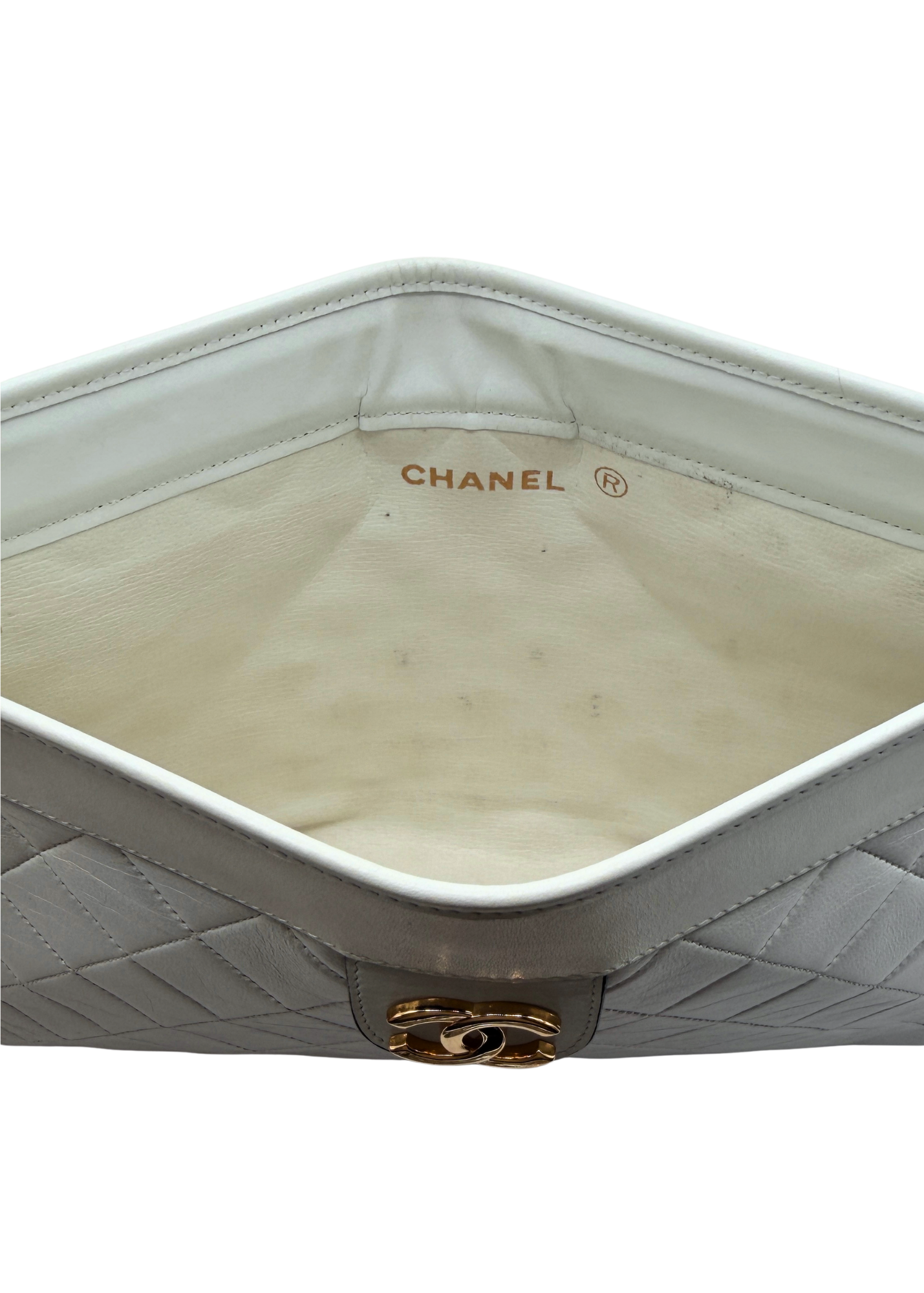 Close-up of a vintage Chanel clutch handbag with quilted design and gold hardware on a white background