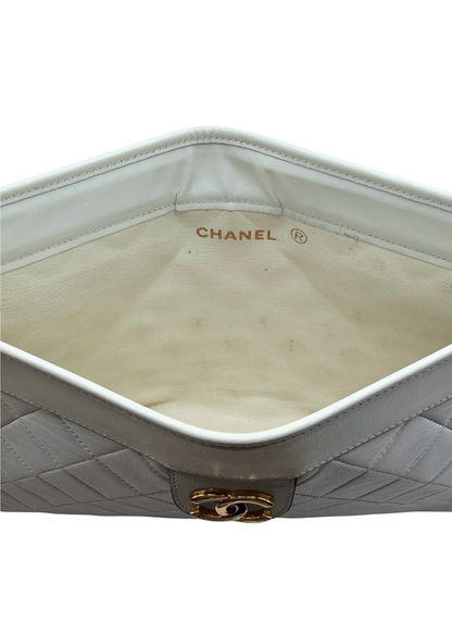 Close-up of a vintage Chanel clutch handbag with quilted design and gold hardware on a white background