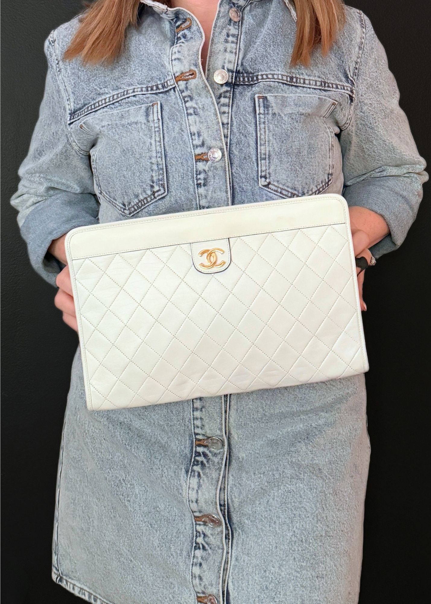 Person holding a white vintage Chanel quilted handbag with a gold logo on a black background