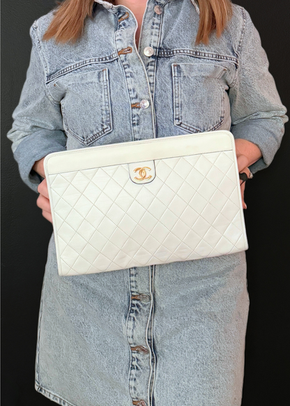 Person holding a white vintage Chanel quilted handbag with a gold logo on a black background