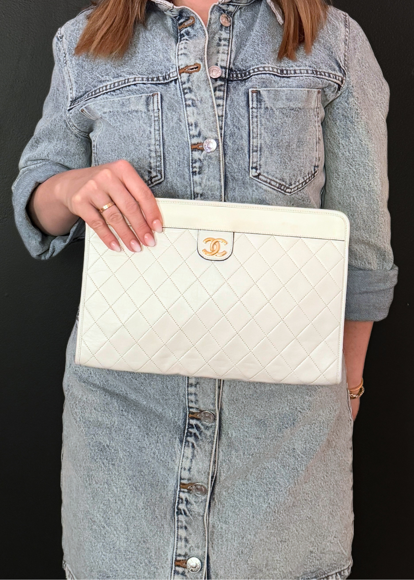 Person holding a white vintage Chanel quilted handbag with a brand logo against a black background