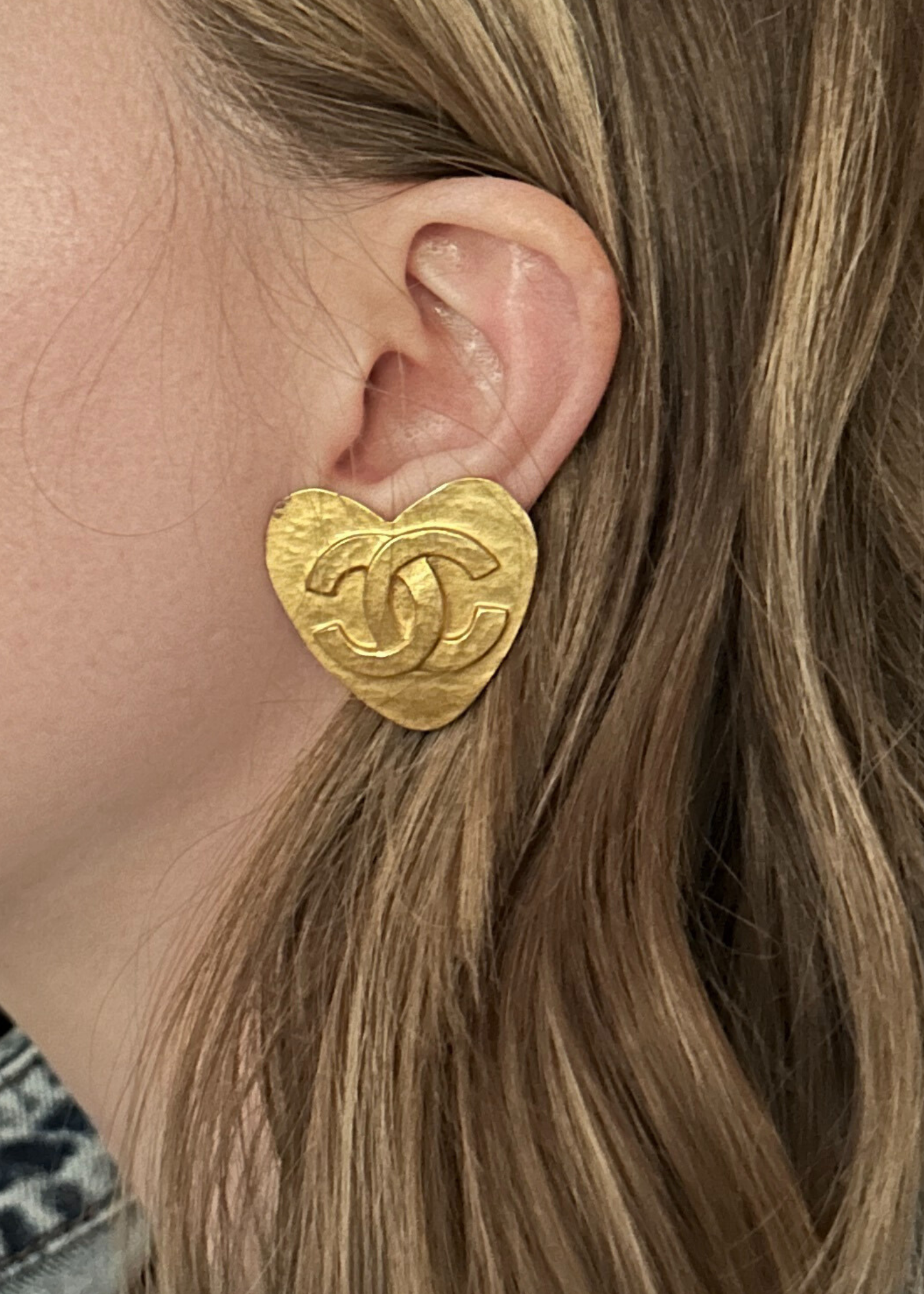 Gold heart-shaped Chanel earring worn by a person with blonde hair.