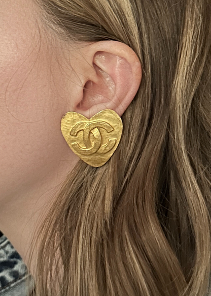 Gold heart-shaped Chanel earring worn by a person with blonde hair.