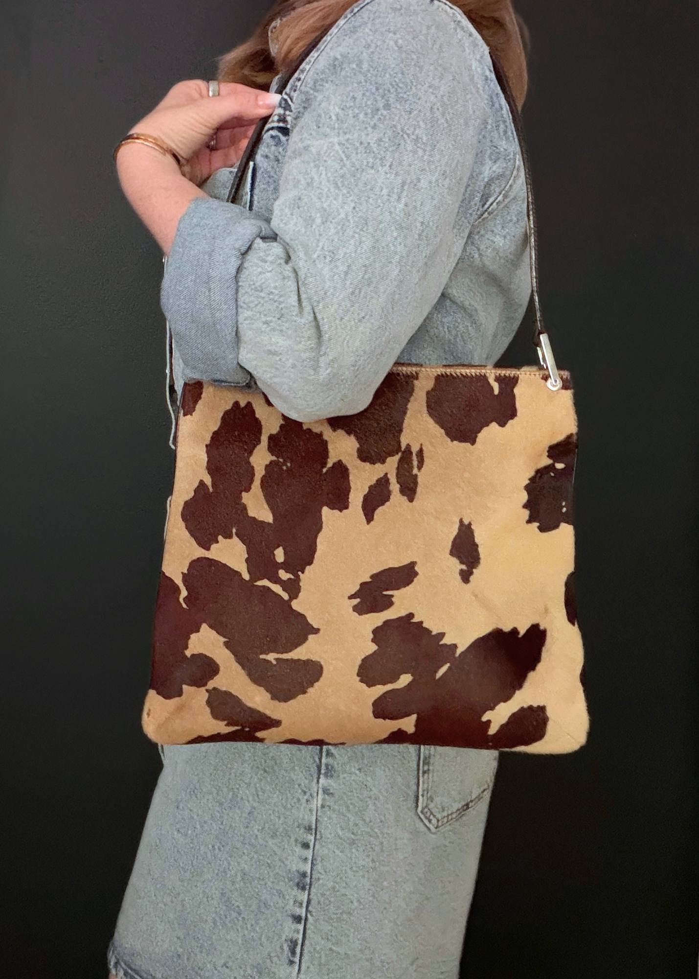 Person holding a brown and beige vintage Fendi cow print bag against a black background