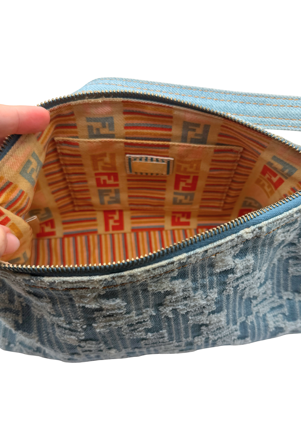 A close-up of a Fendi vintage with a distressed blue denim zucca exterior and a patterned interior featuring the signature Fendi FF logo in red, orange, and blue on a beige background.