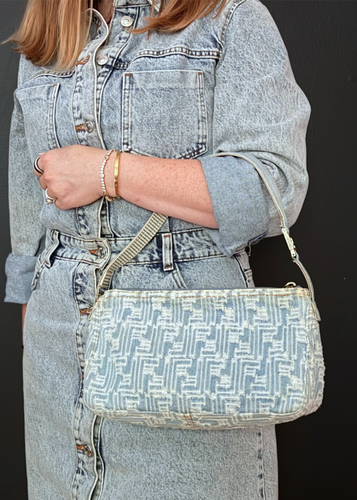 A person wearing a light-wash denim dress holds a vintage Fendi zucca denim light blue and white shoulder bag with a matching strap against a dark background.