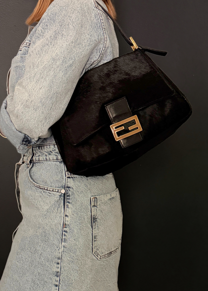 Person wearing a black handbag with gold accents on a dark background