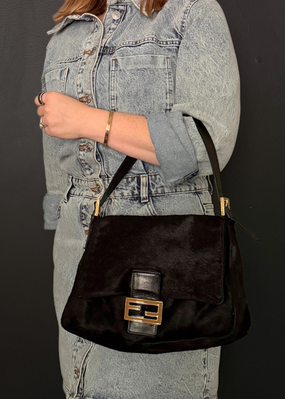 Person wearing a black handbag with gold accents against a dark background