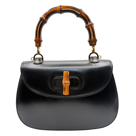A black leather Gucci handbag with a curved bamboo handle and a bamboo-shaped turn-lock clasp on the front flap, shown against a plain white background.