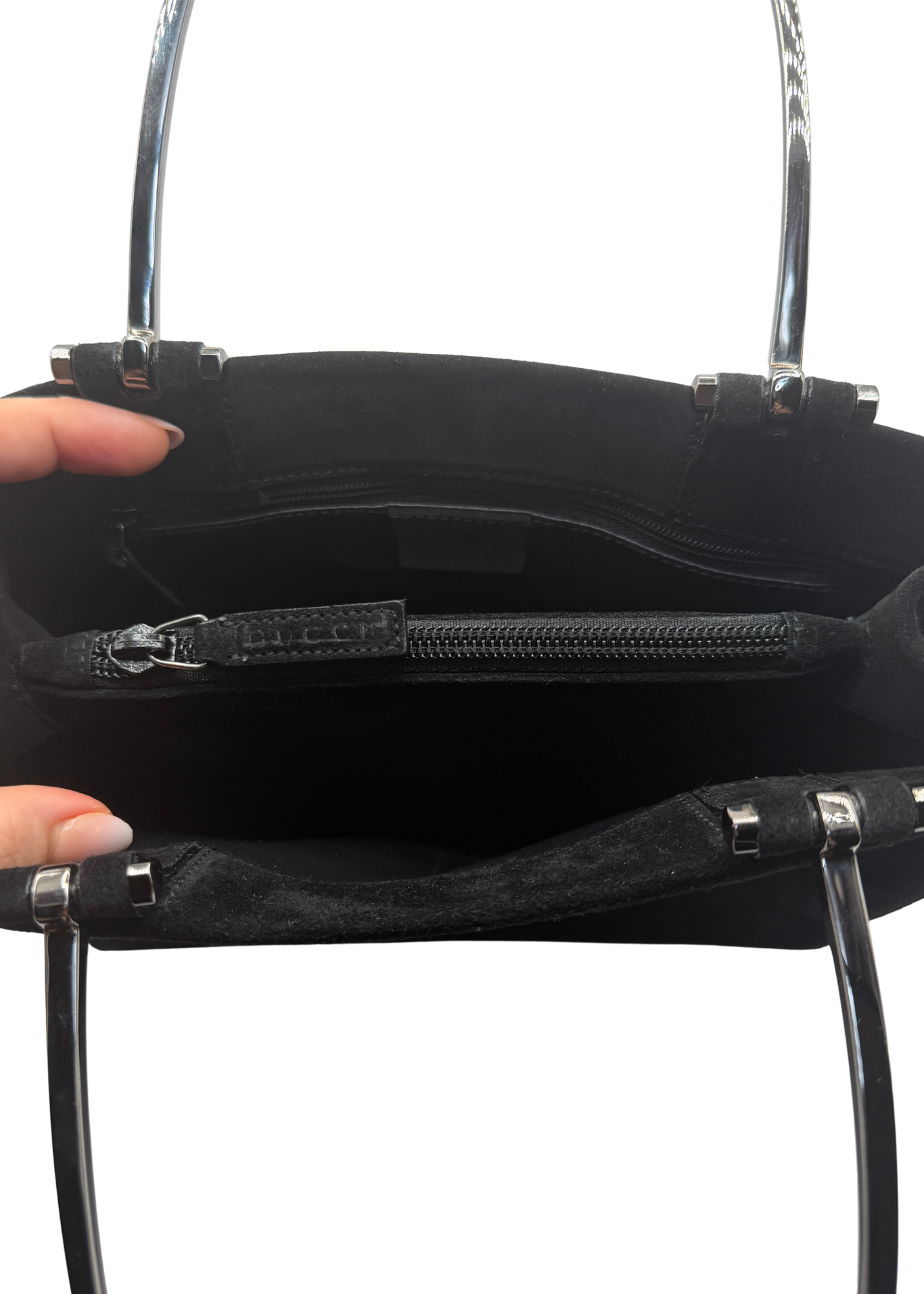 Black Gucci tote bag shown open, with a hand holding the left side to display the interior. The bag features a black suede-like exterior, a black zippered pocket, and silver-tone metal hardware with Gucci branding on the zipper pull.