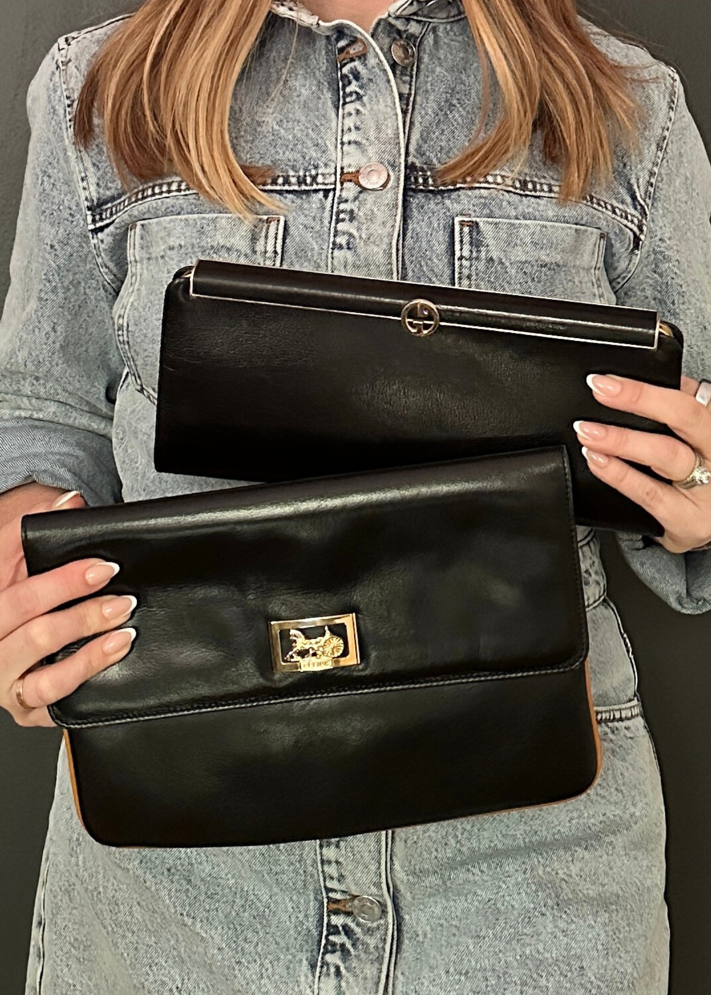 Person holding two black handbags with gold accents against a gray background