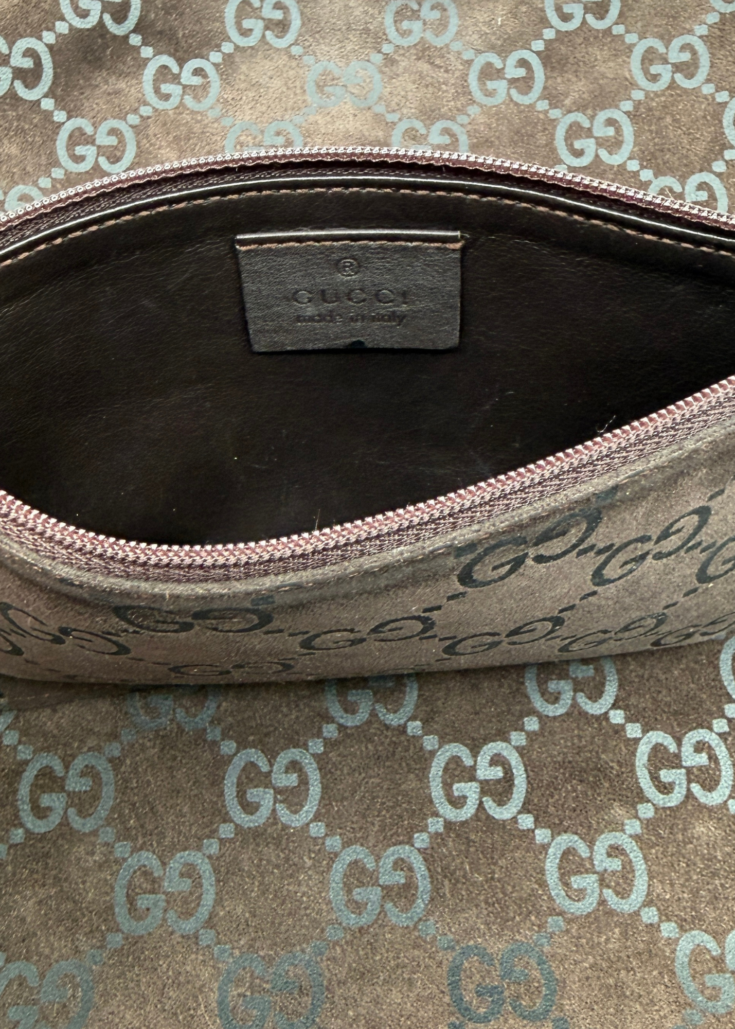 Close-up of an open Gucci zip pouch showing the interior lining and a Gucci leather label inside, with the exterior featuring the classic brown and beige GG monogram canvas.