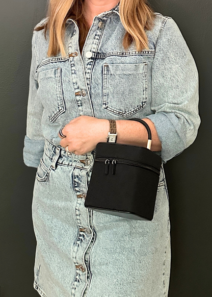 Person wearing a light blue denim dress holding a black handbag against a dark background