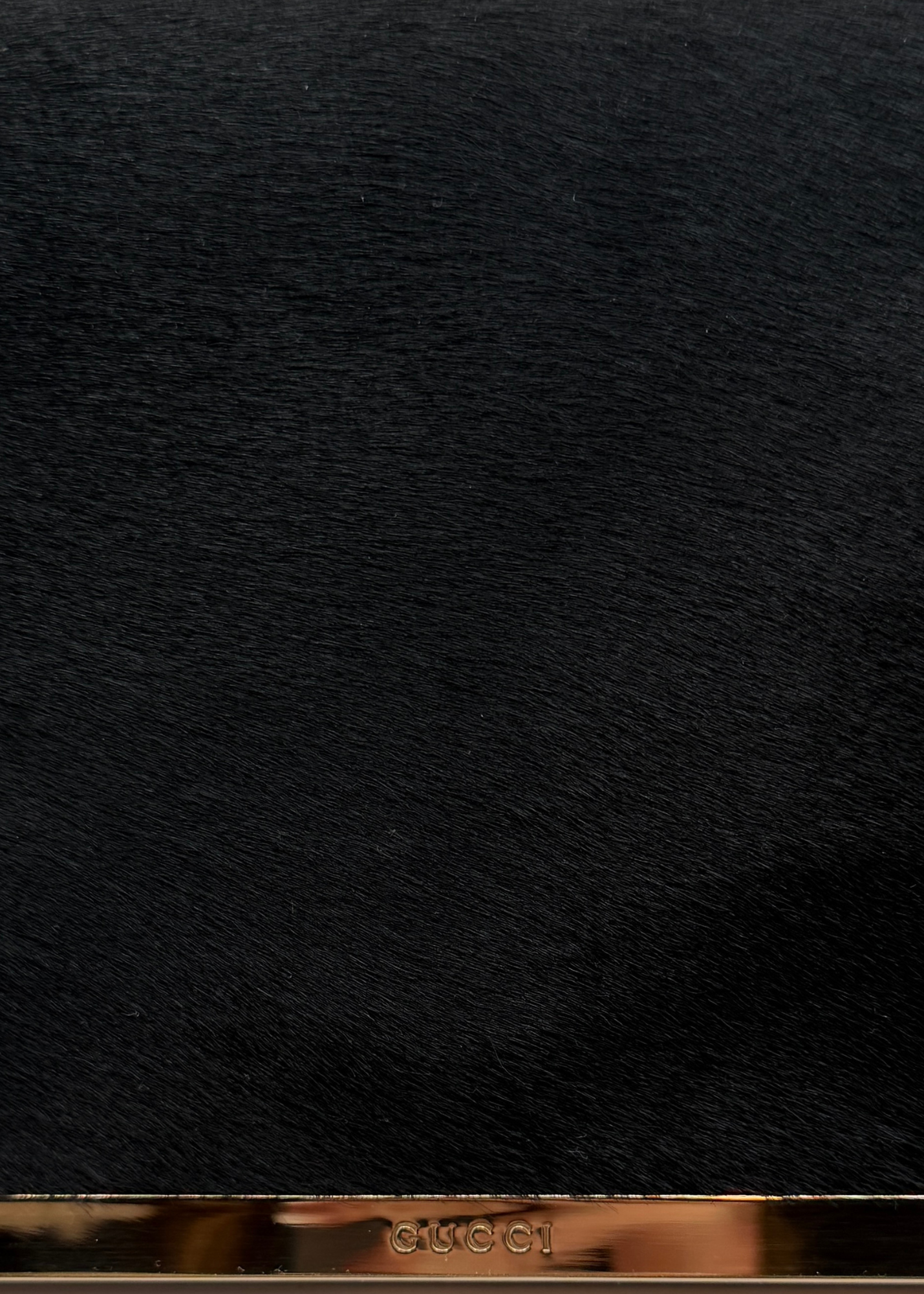 Close-up of a textured black ponyhair vintage clutch surface with 'Gucci' branding at the bottom.