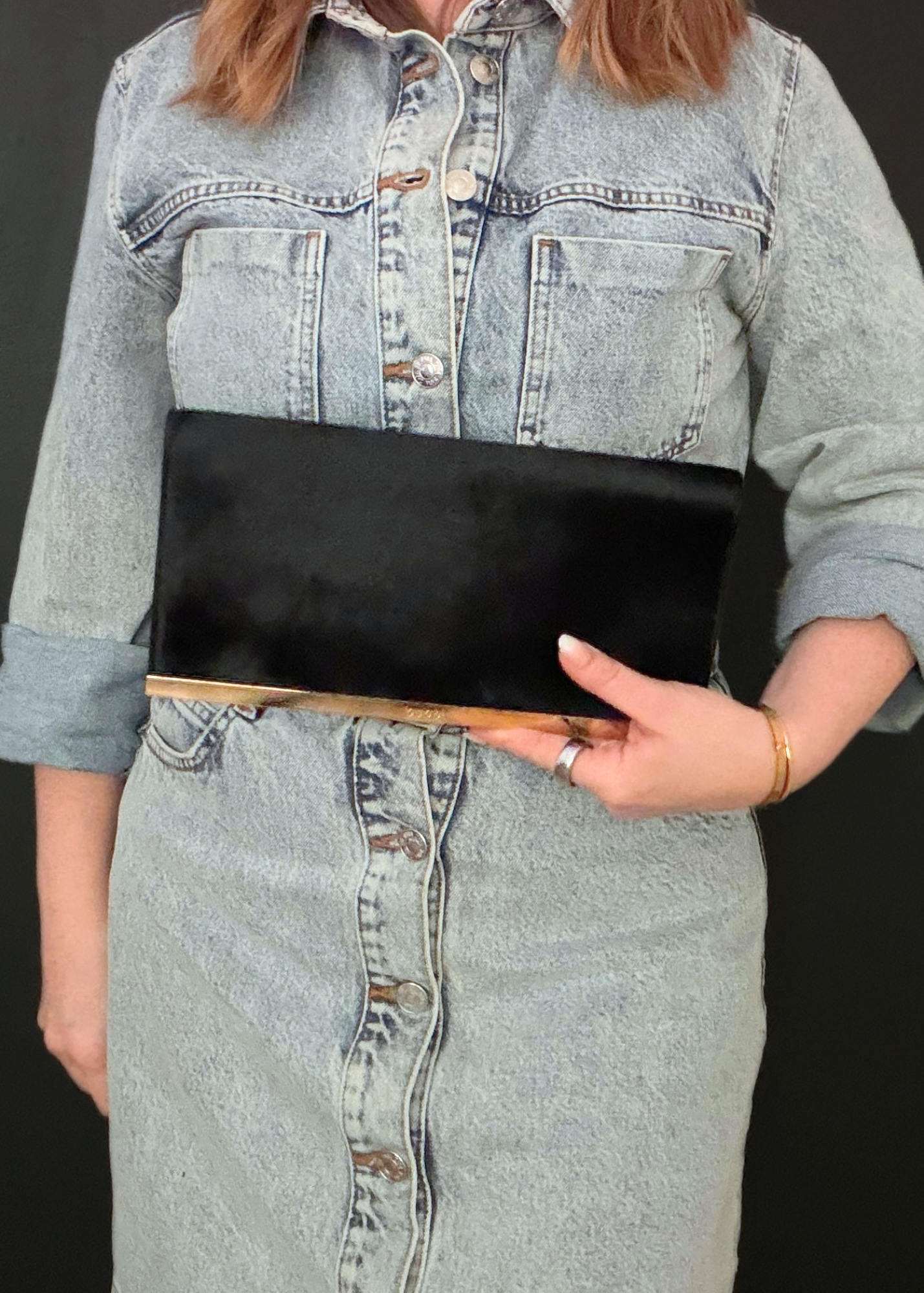 Person wearing a denim outfit holding a black vintage Gucci clutch against a dark background