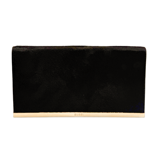A black ponyhair vintage Gucci clutch bag with a gold-tone metal trim featuring the embossed brand name 'GUCCI' in gold lettering, set against a plain white background.