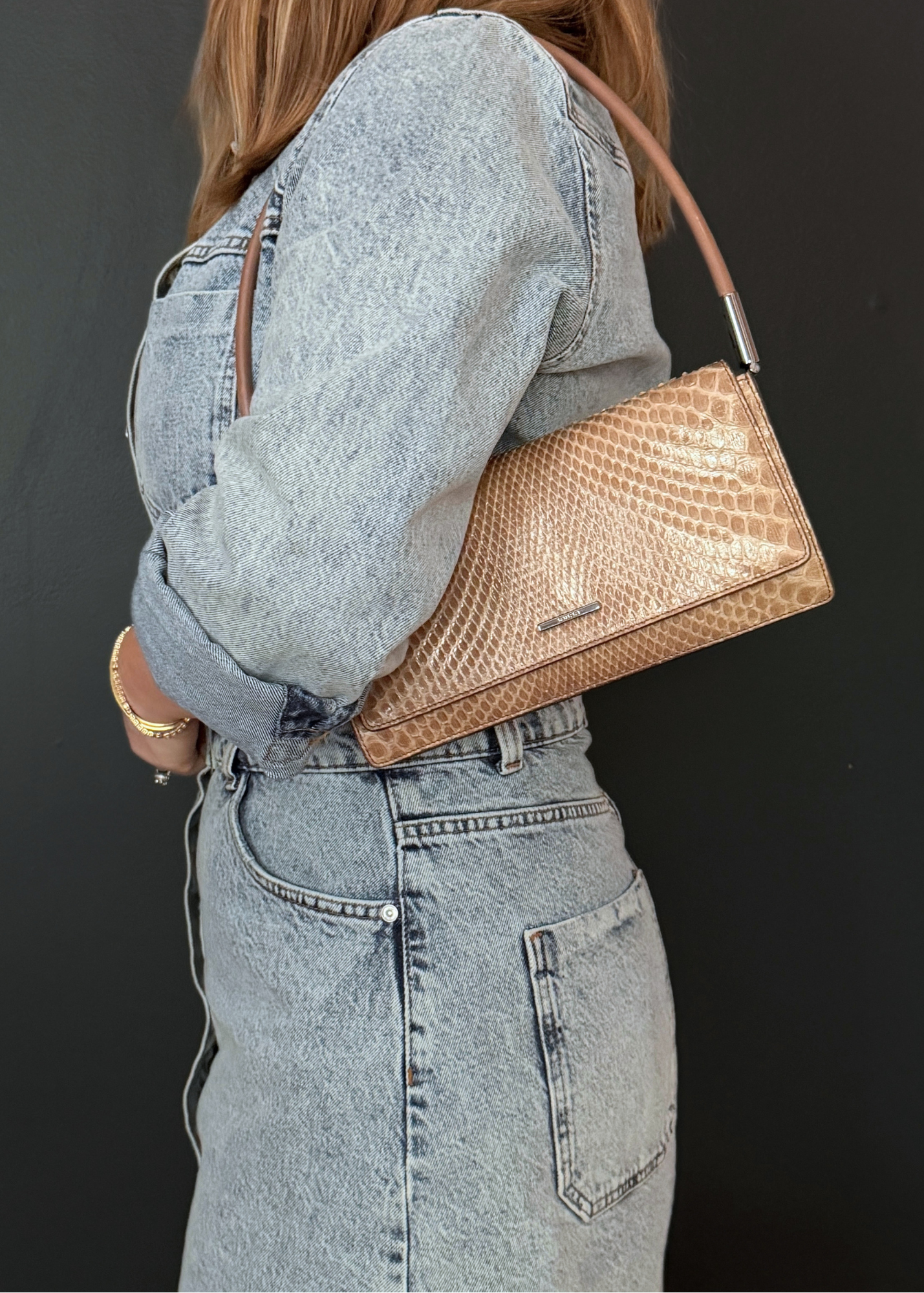 Person wearing a denim outfit with a tan vintage Gucci python leather handbag on a dark background
