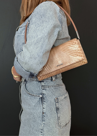 Person wearing a denim outfit with a tan vintage Gucci python leather handbag on a dark background