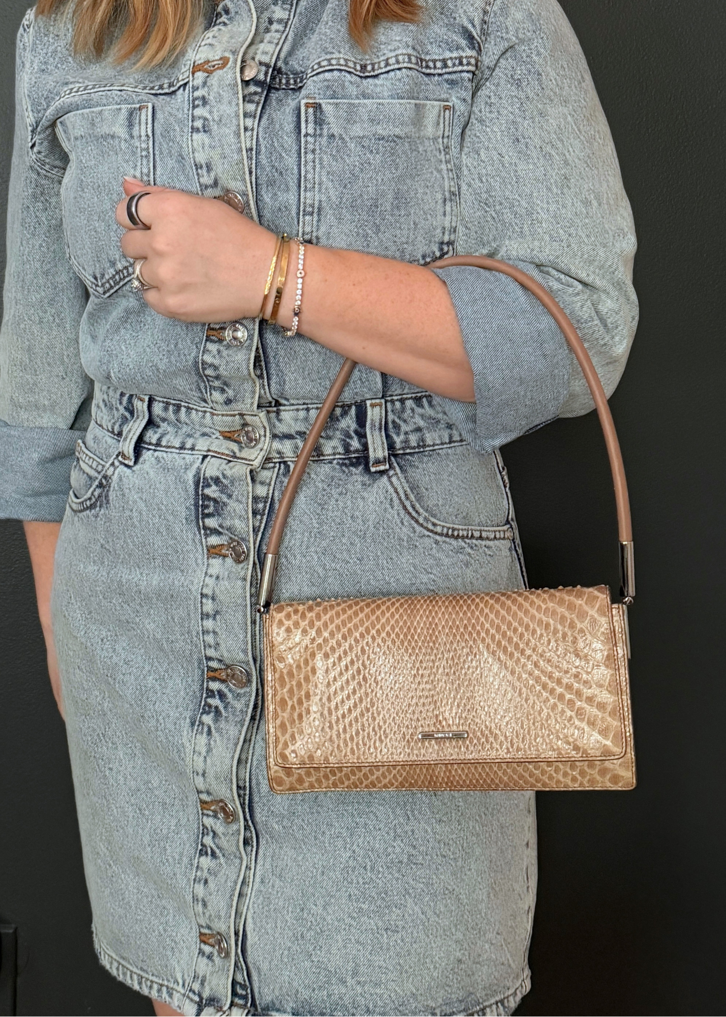 Person wearing a denim outfit with a tan python leather vintage Gucci handbag on a black background