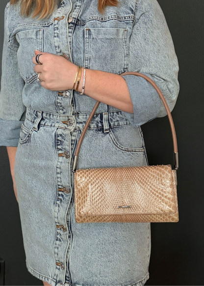 Person wearing a denim outfit with a tan python leather vintage Gucci handbag on a black background