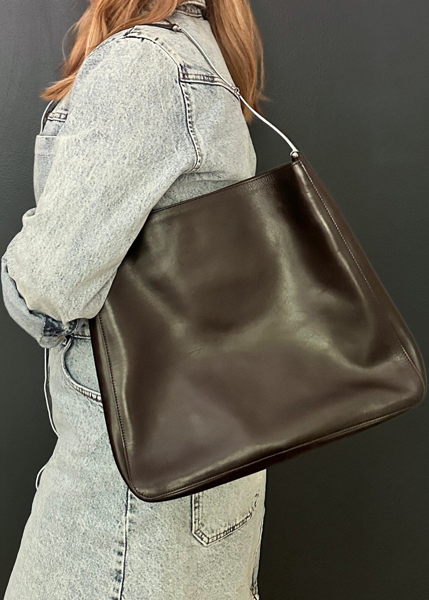Person wearing a brown leather handbag against a dark background