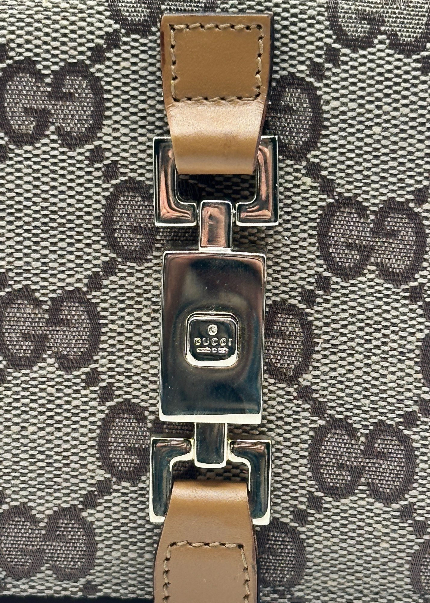 Close-up of a Gucci bag with monogram pattern and brown leather strap.