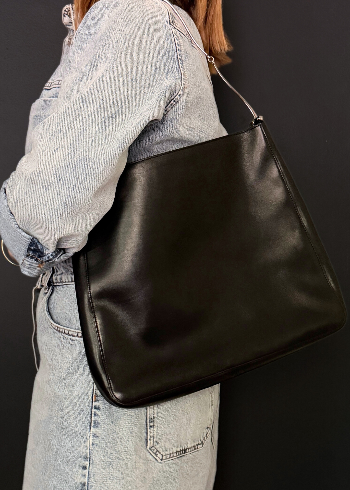 Person wearing a vintage Gucci black leather shoulder bag against a dark background