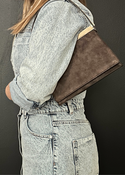 Person wearing a gray jacket with a brown leather clutch against a dark background