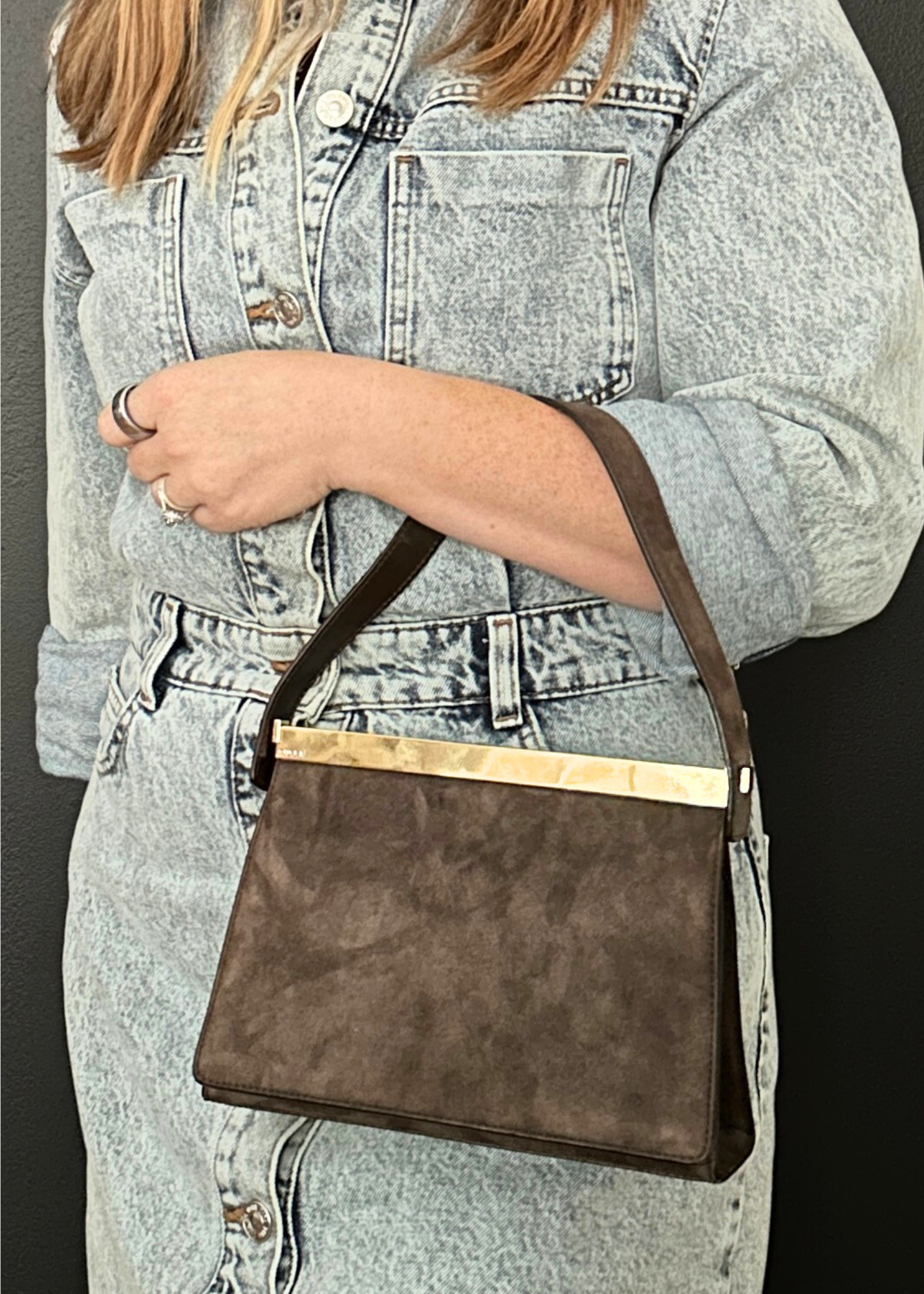Person holding a brown handbag with a gold accent against a dark background